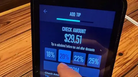 AFP via Getty Images A customer choosing what level of tip to pay at a restaurant in the US