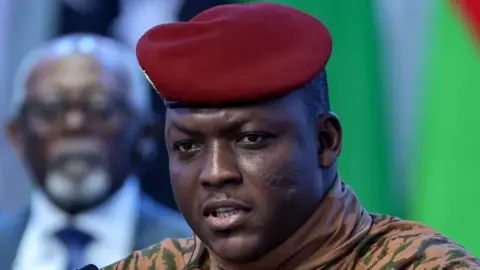 TASS via Reuters Ibrahim Traoré is pictured close up in beige military fatigues and red beret.