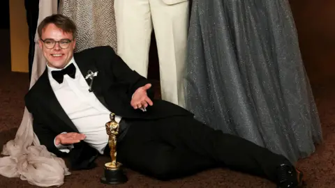 Reuters A man in a tuxedo lies on the floor in front of a golden Oscar statuette