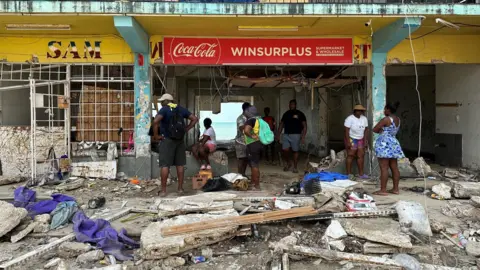 Brandon Drenon / BBC People are searching through debris and damaged stores for supplies 
