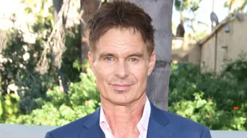 Getty Images Patrick Muldoon wearing a white open-necked shirt and blue suit jacket