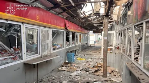 Reuters Photo provided by the Ukrainian prosecutor's office showing badly damaged indoor market area - a corridor with kiosks on either side with broken windows, and metal and glass strewn across the floor.