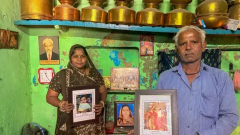 Zoya Mateen Prahlod Thakur (left) and his daughter hold up photos of Sarlaben and Aadhya in their home 