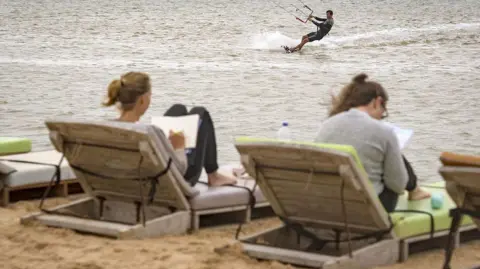 AFP via Getty Images Two European holidaymakers lie on sunloungers in Western Sahara, while another kite surfs in the sea
