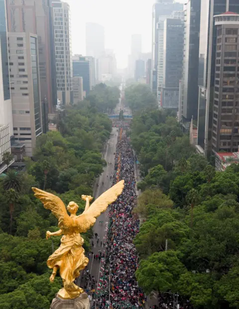 Reuters A drone view of a huge crowd of people on a street lined with trees in an urban setting, with a golden statue in the foreground