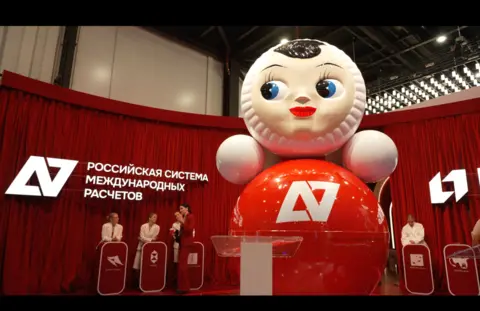 A giant Russian tumbler doll with a red body and blue eyes looking to the left, on display