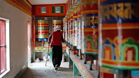 A woman walks past colourful prayer wheels depicting murals from the Buddha's life inside the Kirti monastery
