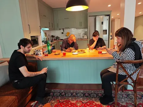 Getty Images Two men and two woman sit around a kitchen table in a Tehran apartment checking their phones