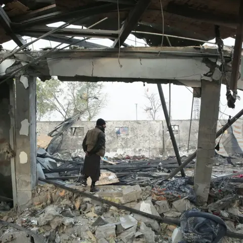 EPA A man stands in the burnt wreckage of the rehabilitation facility. His back is ot the camera. The walls are blackened. Sky can be seen through the broken roof, there is rubble on the floor.