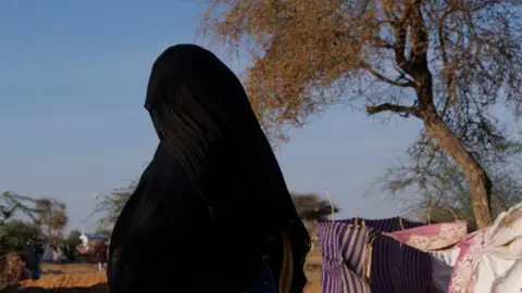 Getty Images An unidentified woman wearing an abaya and hijab walks through a camp in Chad. Her face is not visible.