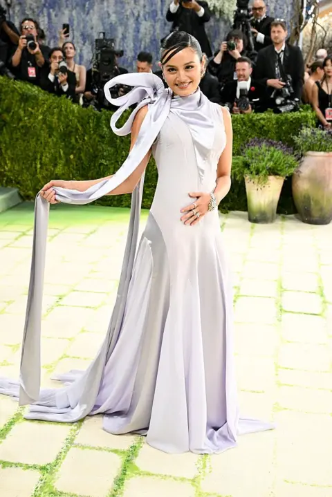 Getty Images Chase Sui Wonders wears a lavender gown with panels in alternating fabrics. She holds a long piece of fabric emanating from her neck bow in her right hand.