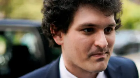 Reuters A close-up shot of Sam Bankman-Fried as he exits a car and heads into a courtroom wearing a dark blue suit jackets, white shirt and necktie.