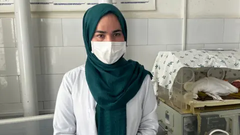 Imogen Anderson/BBC Nurse Fatima Husseini wears a mask and stands next to an premature baby in an incubator 