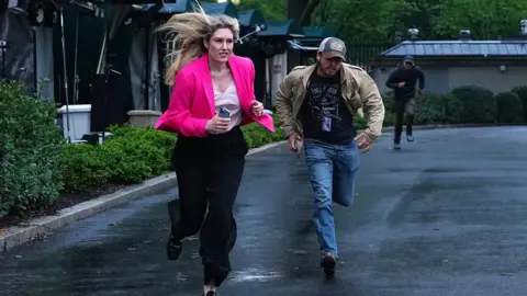 Bloomberg via Getty Images Members of the media clear the North Lawn following reports of gunfire near the White House. A blonde woman is pictured running while wearing a bright pink blazer.