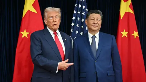 Getty Images Donald Trump (L) and Xi Jinping (R), both wearing blue suits, stand between two Chinese flags, with a US flag between them. Trump is pointing towards Xi with his right hand.