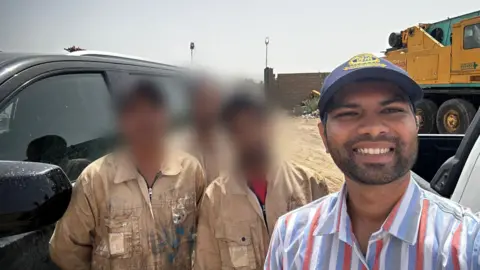 Rex Pereira Rex Pereira standing in a striped shirt with three men in beige overalls standing next to a car 