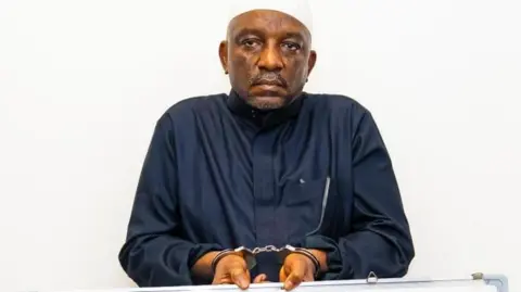 EFCC/X Saleh Mamman wearing a black cloth, handcuffed and holding a white board