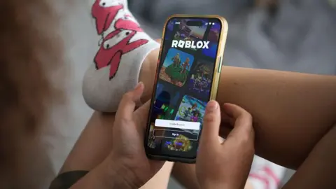 Getty Images Boy sitting down with back to us and leg crossed playing Roblox on phone 