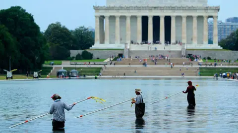 Getty Images Workers with long poles clean the pool with the Lincoln Monument in the background