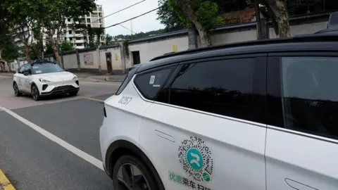 Reuters Two white driverless cars with black hoods are stationary on the road, one behind the other