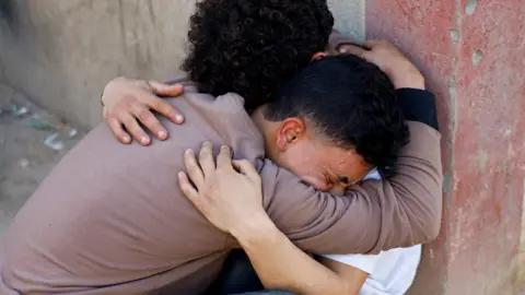 Reuters Two Palestinians mourn after the Israeli military carried out strikes during clashes between Hamas security personnel and Israeli-backed militiamen, at al-Aqsa hospital in Deir al-Balah, central Gaza (6 April 2026)