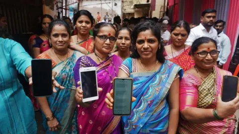 Hindustan Times via Getty Images Women who were beneficiaries of mukhyamantri ladaki bahin yojana showing their bank passbooks and the message of the scheme money received in thier mobile phones at Kisan Nagar on September 10, 2024 in Thane, India. 