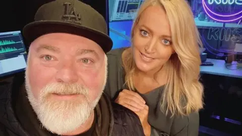 Supplied A middle-aged man with a black baseball cap and grey beard and a blonde-haired younger woman smile at the camera