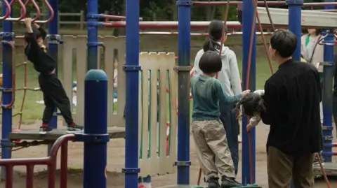 Jiro Akiba/BBC A group of children in a playground where you can see some adults.