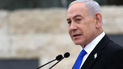EPA Netanyahu, who has grey short hair and wears a black suit with a blue tie and has a badge of the Israeli flag on his lapel, speaks into a mic at a podium