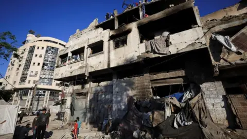 Reuters People walk past a ruined building following an Israeli strike in Gaza City