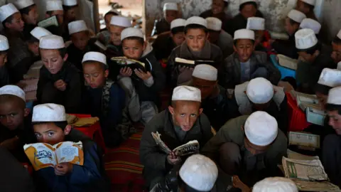 AFP via Getty Images Afghan boys in white hats sit on a rug on the floor and study the Quran at a madrasa, an Islamic school in Argo district, Badakhshan province on May 12, 2026.