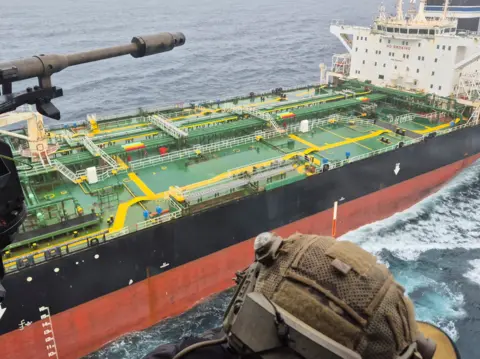Reuters An image from on board a French navy helicopter as it approaches an oil tanker said to be part of Russia's shadow fleet. A navy officer can be seen wearing a camouflage military helmet. 