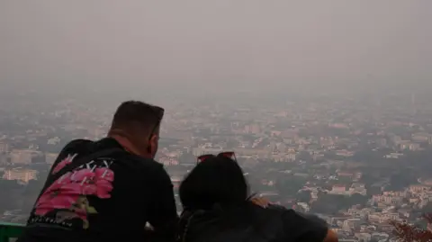BBC/Wasawat Lukharang A couple standing at a lookout point; haze engulfs the landscape in the horizon 