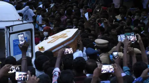 AFP via Getty Images Residents film the white coffin of one of the men in Sathankulam, Tamil Nadu, in 2020.