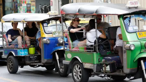 EPA Tourists travel on tuk-tuk taxis in Bangkok.