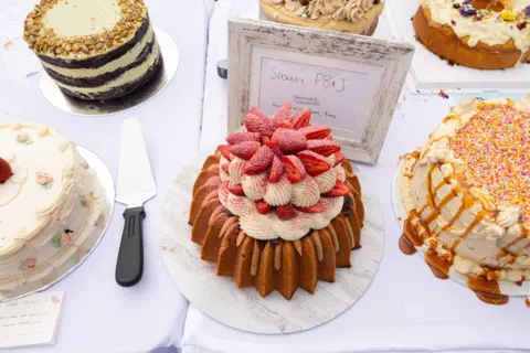 Jessica Hromas/BBC A cream and strawberrry cake (centre) beside a caramel cake with sprinkles on it