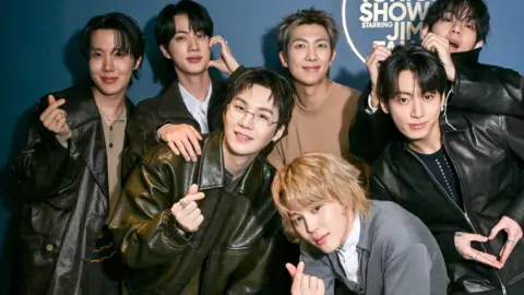 Getty Images J-Hope, Jin, Suga, RM, V, Jung Kook,and Jimin (crouched) of BTS pose together on Wednesday, March 25, 2026