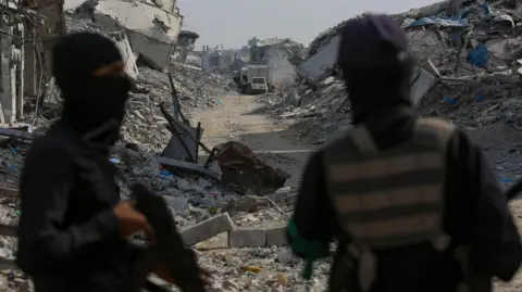 EPA/Shutterstock Fighters of the Al-Qassam Brigades, the military wing of the Hamas movement, stand guard as they search for the bodies of Israeli hostages alongside Red Cross workers in the east of the Gaza Strip, 02 November 2025. 