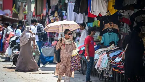 Hindustan Times via Getty Images A woman wearing a beige Indian suit walks holding an umbrella on a sunny afternoon