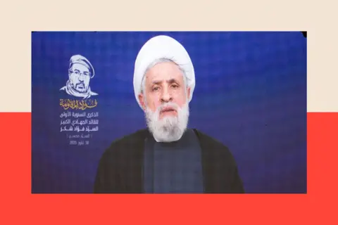 Getty Images Naim Qassem speaks on a screen. He wears black clothes and a white turban.