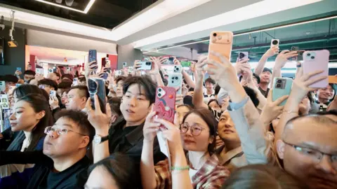 BBC A close-up shot of a crowd waiting to see Wu Yize. Most are holding their phones aloft and craning their necks for a view.