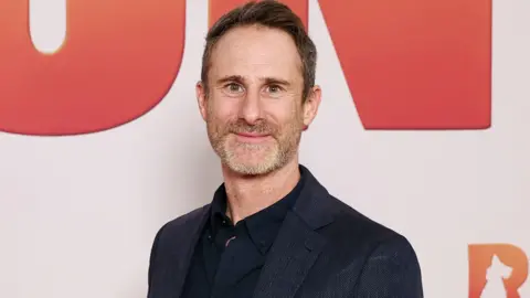 Getty Images A grey-haired man wearing a dark blue suit smiles at the camera.