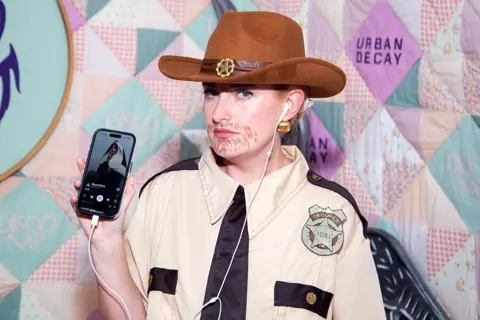 Getty Images Amelia Dimoldenberg shows how she's listening to a Lily Allen song while dressed as a sheriff