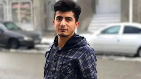 KURDPA Mehrab Abdollahzadeh looks at the camera. He is wearing a blue chequered shirt. 