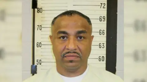 Tennessee Department of Correction A mugshot of Tony Carruthers. He wears a beige shirt, has a mustache, and stares straight ahead. 