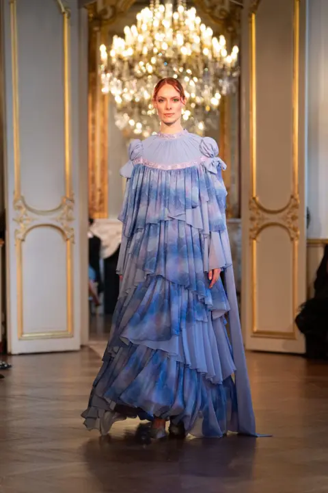 Rooful Ali A long, blue flowy dress designed Hicran Önal exhibited by a ginger model