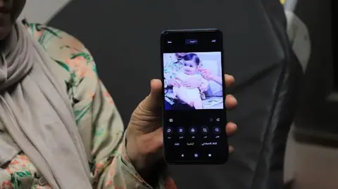 Anadolu via Getty Images A relative holds up a phone showing a photo of Sam Fahd Abu Haikal, a seven month old baby Palestinian boy who was killed by an Israeli bullet in the occupied West Bank on 5 June 2026.