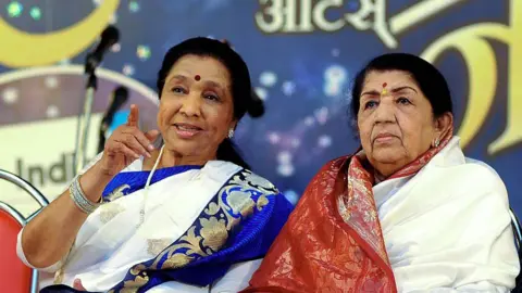 AFP Indian Hindi and Marathi language Bollywood playback singer Lata Mangeshkar (R) speaks with her sister Asha Bhosle also a playback singer during the Pandit Hridaynath Mangeshkar’ Awards in Mumbai late March 31, 2013. AFP PHOTO/STR (Photo credit should read STRDEL/AFP via Getty Images)