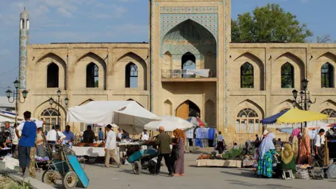 Alamy Uzbekistan, Ferghana valley, Namangan - people shop at market stalls in front of an old medersa