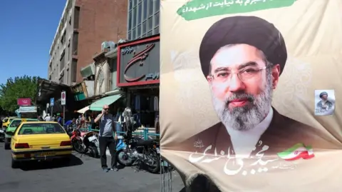 EPA An image of Mojtaba Khamenei in the middle of a road where yellow and green taxis and motorcycles are parked, with a man wearing sunglasses, black trousers and a grey T-shirt holding a phone to his right ear.